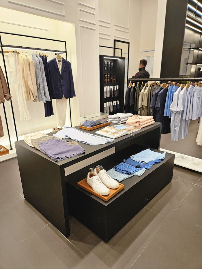 Home Contemporary clothing store showcasing tailored suits, casual shirts, and accessories.